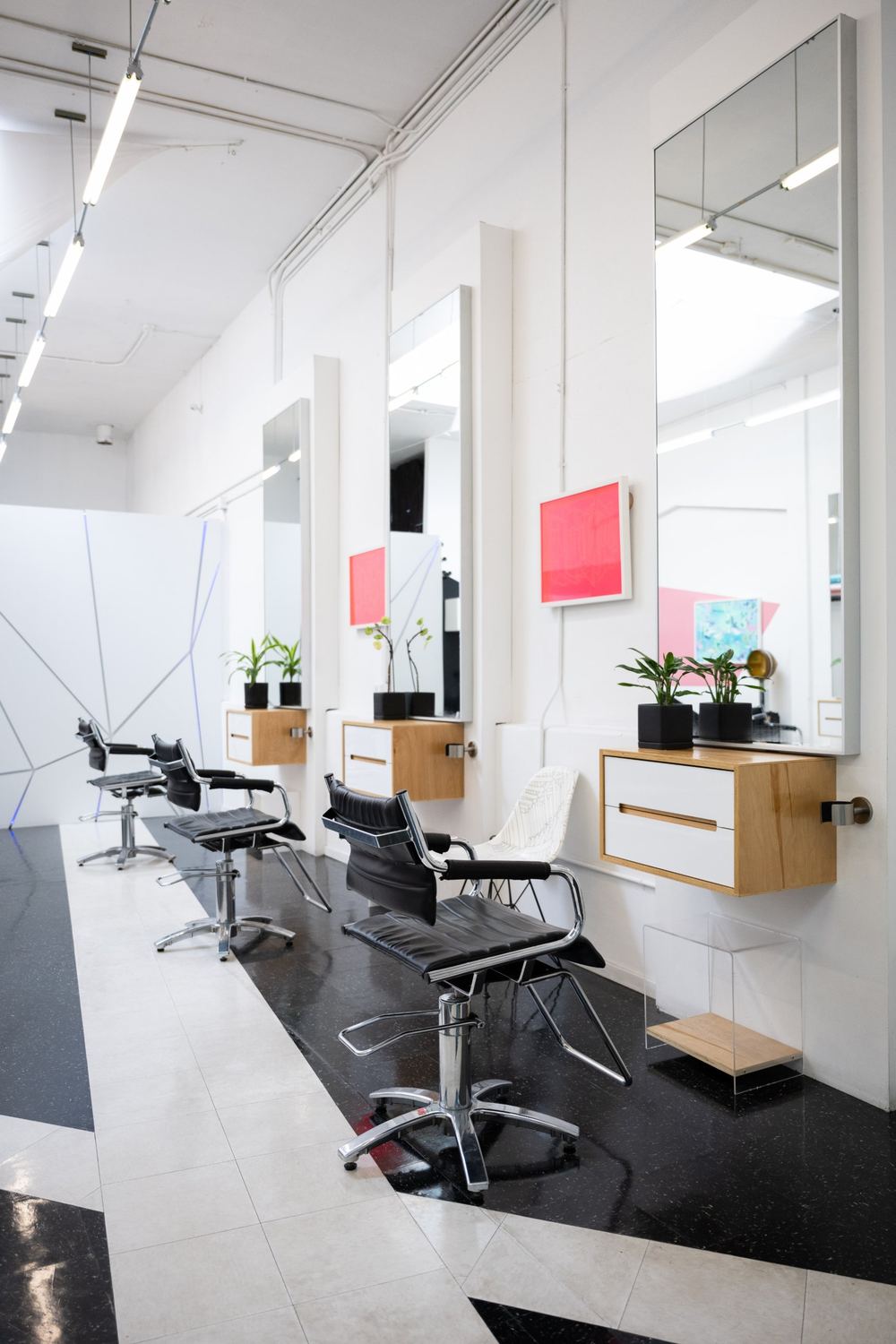 A row of black styling chairs along a wall of mirrors on a black and white floor