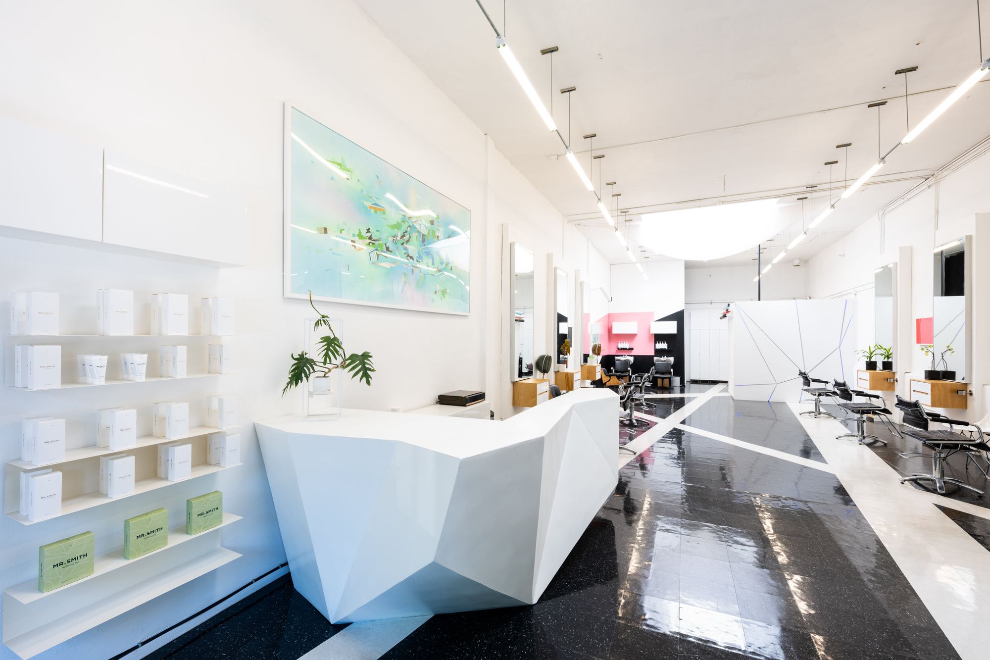 The Cult salon: a faceted white reception desk, product shelves and a row of styling chairs on a black and white floor